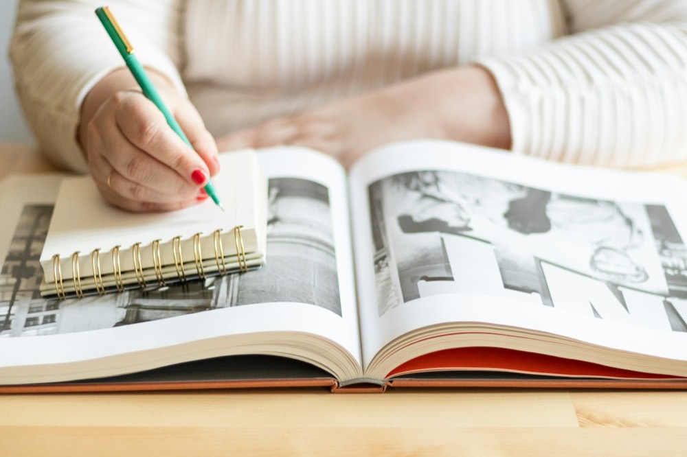 A reader copying notes from a large open book into a spiral notebook