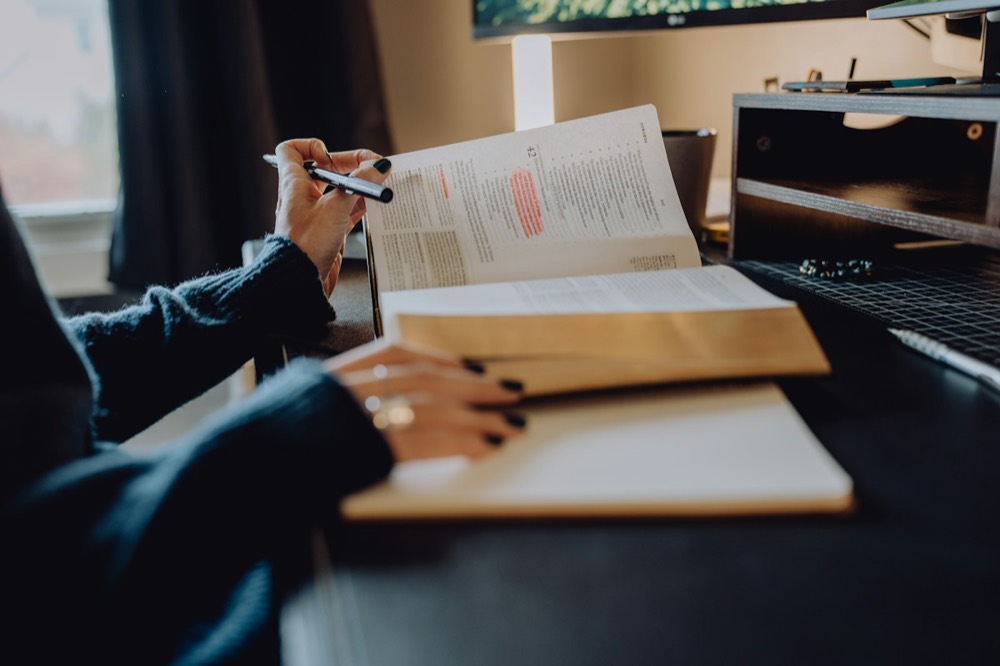 Hands holding a pen over a book page with highlighted passages