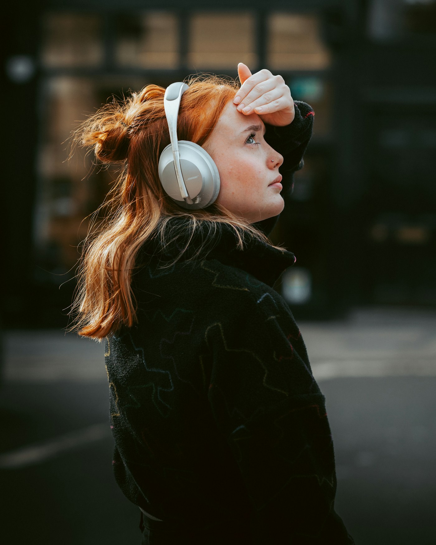 A woman in headphones pausing on a city street, lost in thought