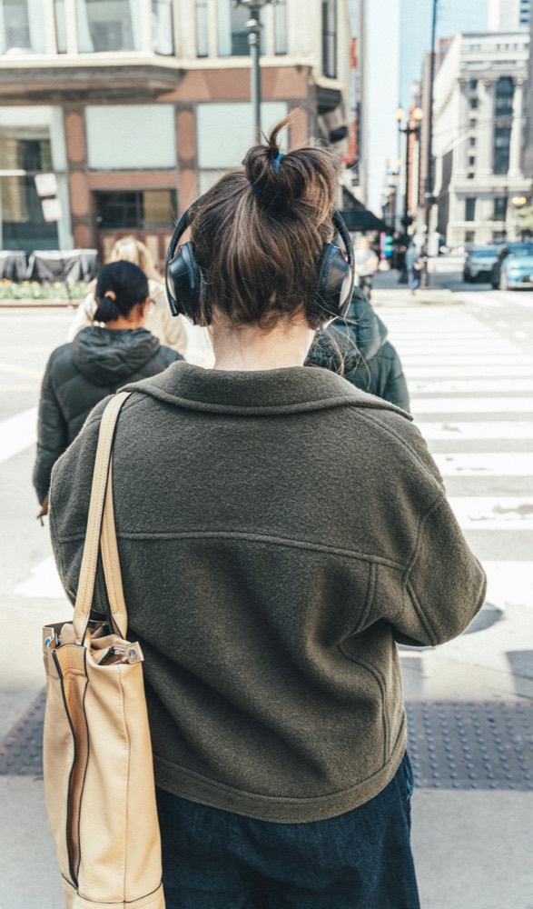 A person in headphones walking away through a city crosswalk