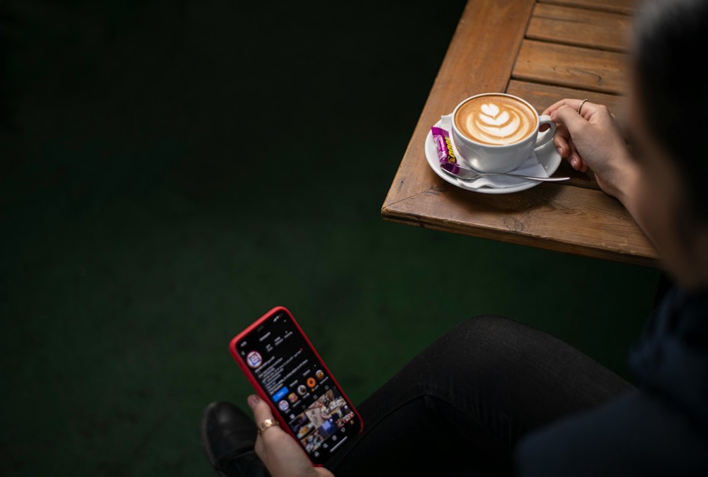A person scrolling on a phone next to a coffee in a dark cafe